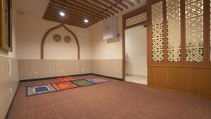 Une salle de prière dotée d’un tapis, de poutres en bois et d’un paravent décoratif.