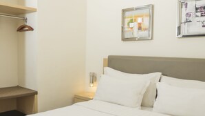 Un lit bien fait, avec du linge de lit blanc, une tête de lit en bois et une table de chevet sur laquelle se trouve une lampe.