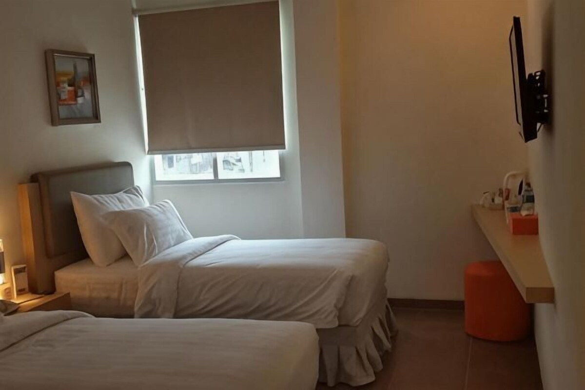 Una camera da letto con due letti, una finestra con tenda, un comodino e una TV a parete.
