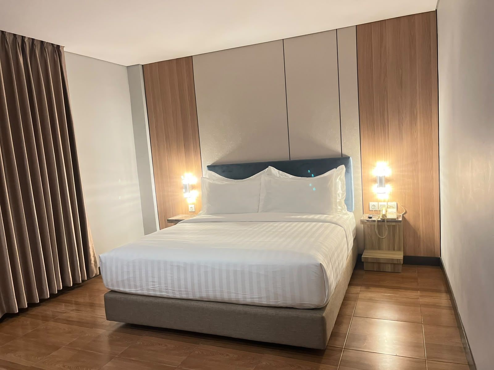 Una habitación de hotel moderna con una cama grande, paneles de madera y una mesita de noche con lámpara.