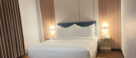 Una habitación de hotel moderna con una cama grande, paneles de madera y una mesita de noche con lámpara.