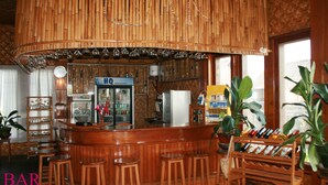 A bar area with a wooden bar counter, stools, a refrigerator, and shelves with bottles. - Golden Island Cottages Nampan Hotel (Nyaungshwe)