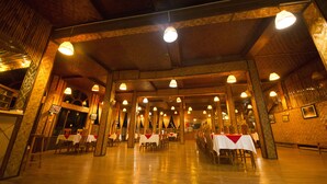 A spacious hall with high ceilings and wooden beams, featuring tables set for dining and multiple hanging light fixtures. - Golden Island Cottages Nampan Hotel (Nyaungshwe)