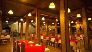 A restaurant with wooden beams, tables with red tablecloths, and hanging lamps. - Golden Island Cottages Nampan Hotel (Nyaungshwe)