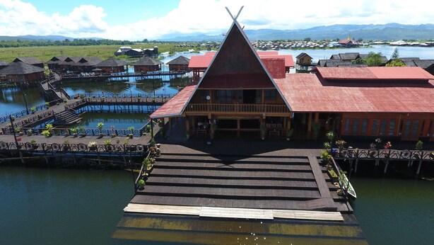 A resort with a prominent triangular building, wooden walkways over water, and a view of the surrounding landscape. - Golden Island Cottages Nampan Hotel (Nyaungshwe)
