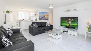A modern living room with a black sofa, a glass coffee table, and a flat-screen TV. - 112 Olive Apartments (Mildura)