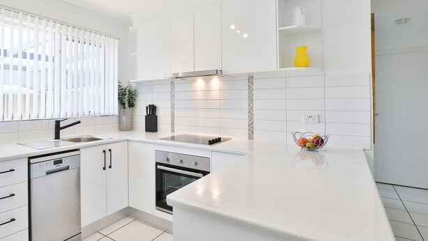 A modern kitchen with white cabinetry, a dishwasher, an oven, and a countertop with a fruit bowl. - 112 Olive Apartments (Mildura)