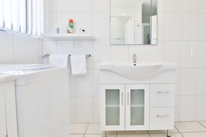 Casa de banho moderna com lavatório branco, armários com portas de vidro e espelho sobre o lavatório.