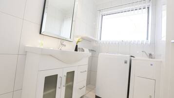 A modern bathroom with a white sink, mirror, and a window with blinds.