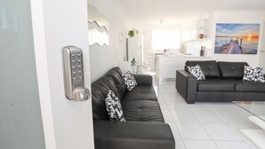 A modern living room with a black leather sofa, a glass coffee table, and a white wall-mounted telephone. - 112 Olive Apartments (Mildura)
