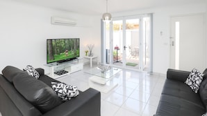A modern living room with a flat-screen TV, two black leather sofas with patterned cushions, a glass coffee table, and a sliding glass door leading to a patio. - 112 Olive Apartments (Mildura)