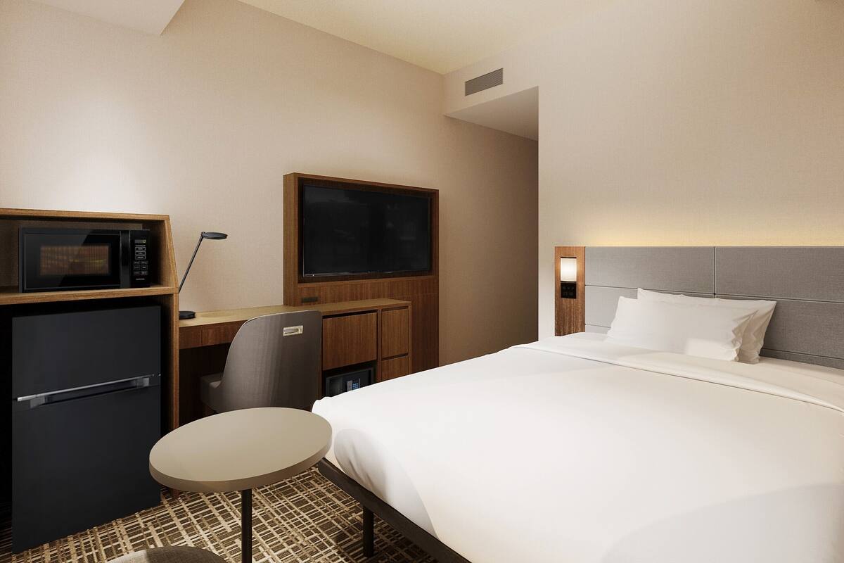 Une chambre d’hôtel comprenant un lit, un bureau avec un micro-ondes, une télévision et une petite table.