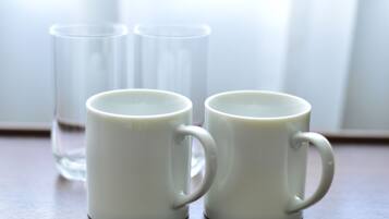 Two white ceramic mugs on a wooden surface with a clear glass in the background.