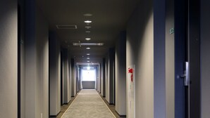 Un long couloir étroit d’hôtel, avec un tapis à motifs, des luminaires encastrés et des portes de part et d’autre.