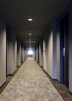 A long, narrow hotel corridor with a patterned carpet, recessed lighting, and doors on both sides.