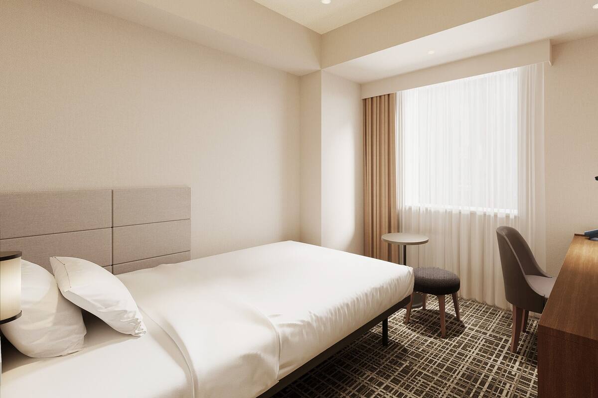 Une chambre d’hôtel avec un lit, un bureau, une chaise et une fenêtre avec des rideaux.