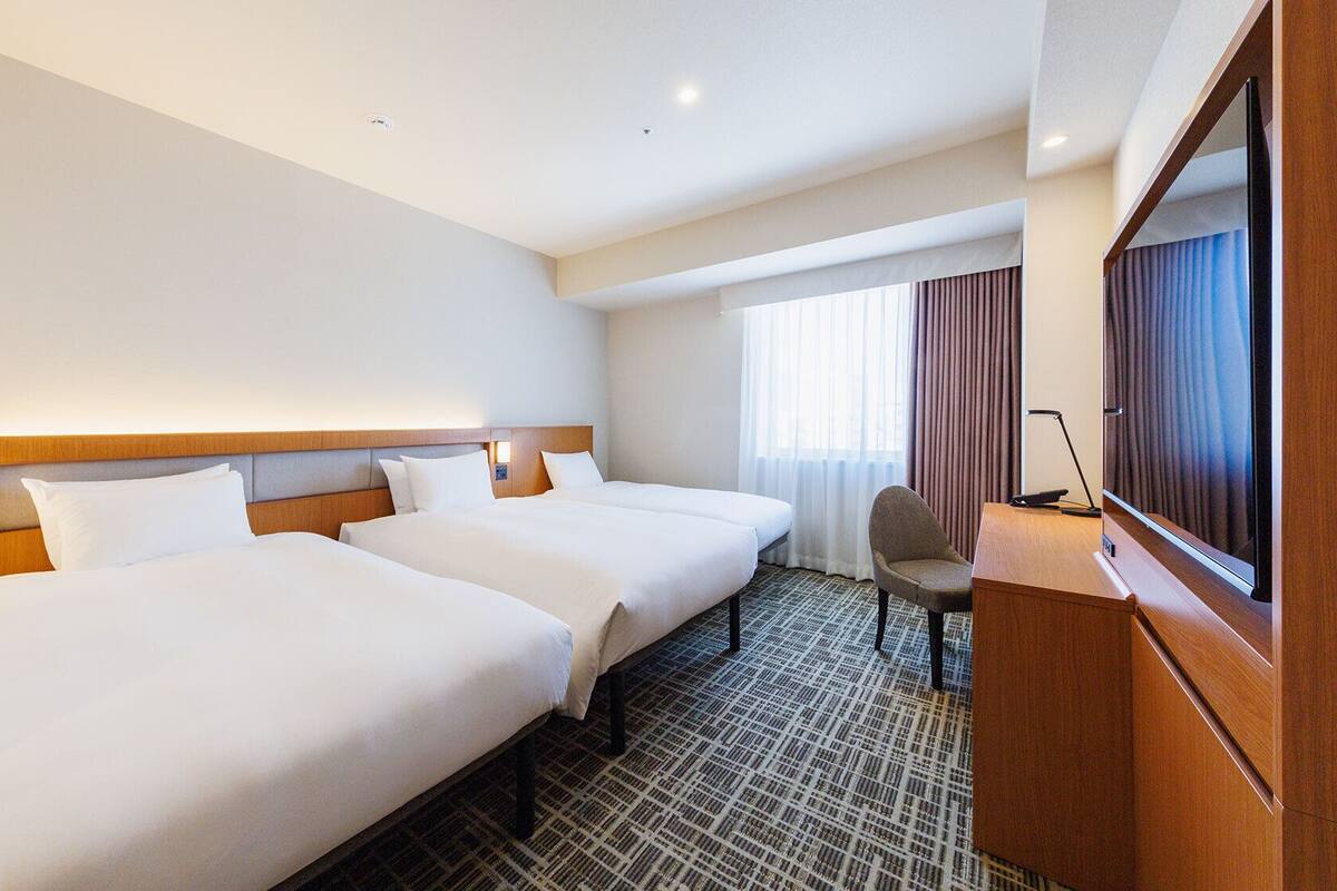 Une chambre d’hôtel avec deux lits, un bureau, une chaise, une télévision et une fenêtre avec des rideaux.
