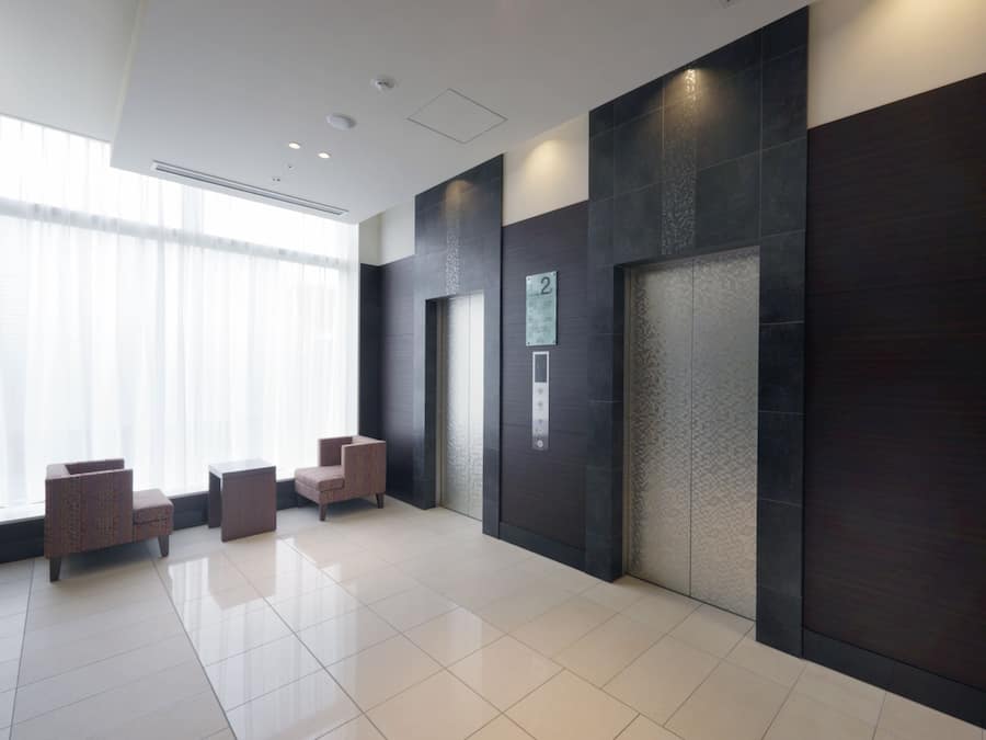 A modern lobby with a reception desk, seating area, and an elevator.