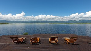 Une terrasse en bois avec quatre chaises en bois, donnant sur un lac paisible, entouré de montagnes et surplombant un ciel dégagé.