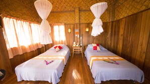 A room with two beds, wooden walls, and a central table with a lamp. - Golden Island Cottages Thale-U Hotel (Nyaungshwe)