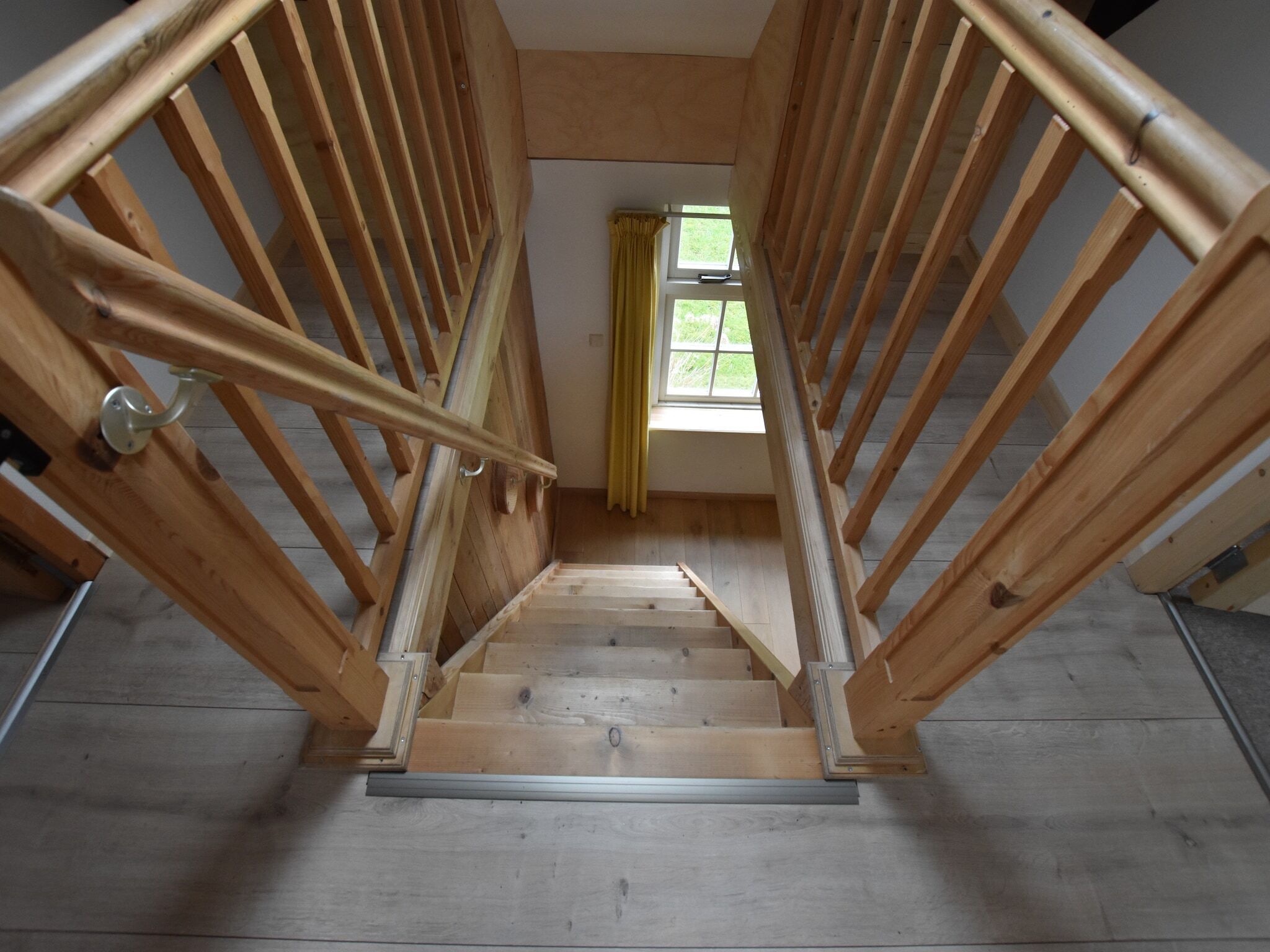 A wooden staircase with a handrail, leading to a window with yellow curtains.