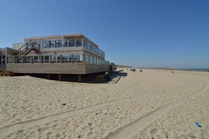 A beachside building with a wooden deck and a staircase leading to the upper level.