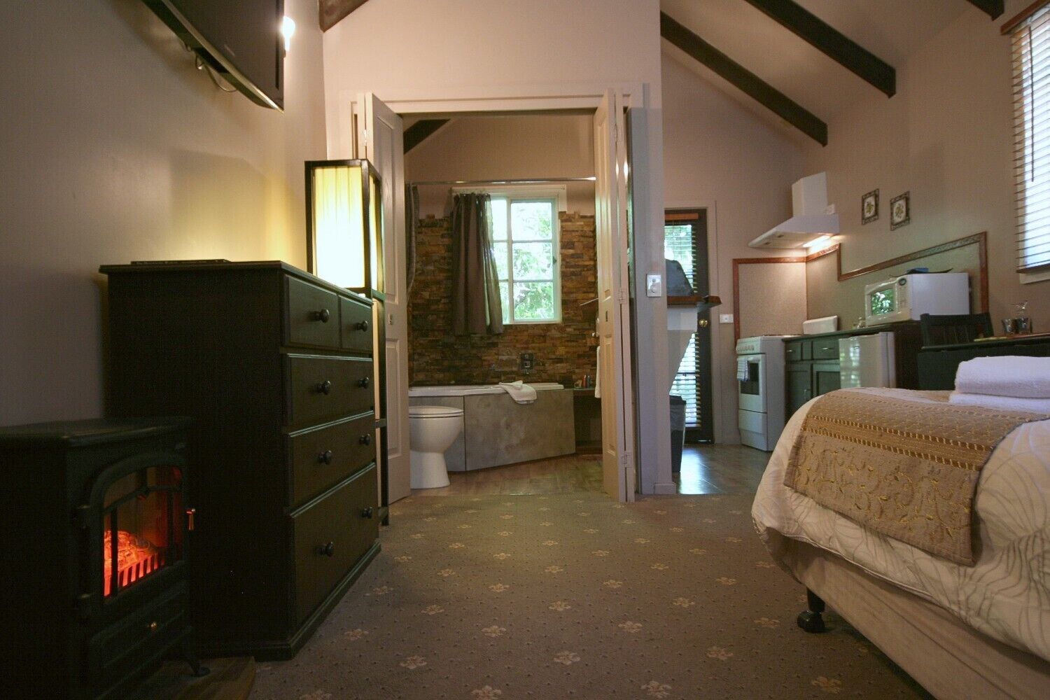 Un dormitorio con cama, cómoda, chimenea, baño con ducha y zona de cocina.
