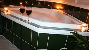 A spa tub with two glasses of red wine and candles.