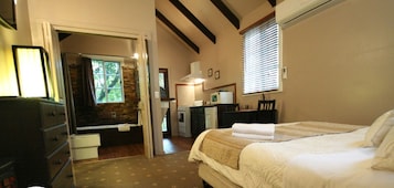 Quarto com cama, cômoda, escrivaninha com cadeira, janela com persianas e parede de pedra.