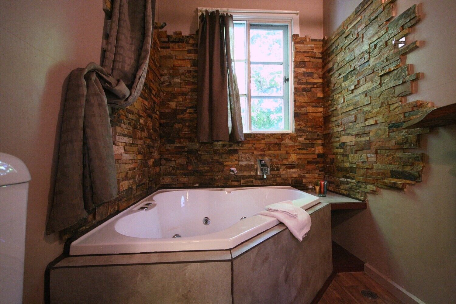 Une salle de bain avec un mur en pierre, une fenêtre, une baignoire et une serviette accrochée au mur.