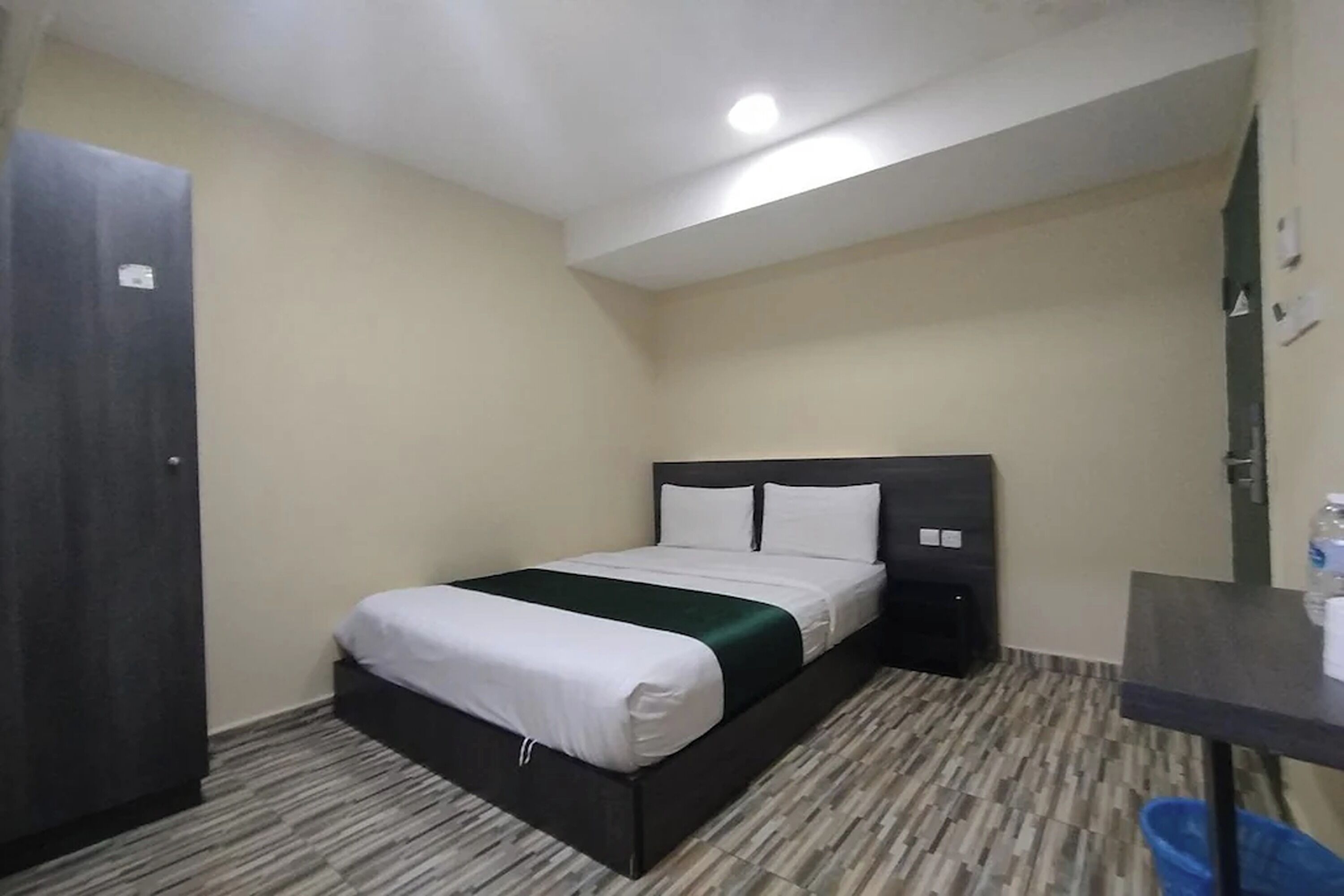 A small, neatly arranged hotel room with a bed, a desk, and a wardrobe.