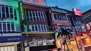 Un hôtel avec une enseigne au néon, un restaurant KFC et un magasin Guardian.