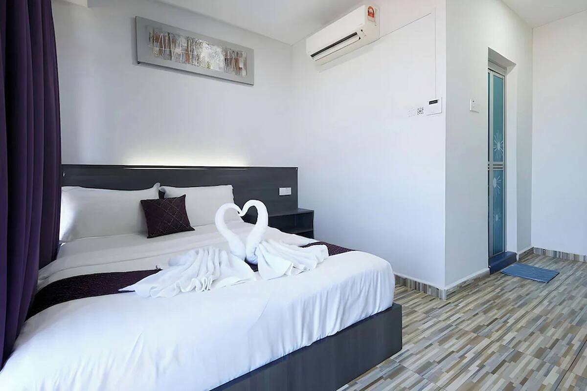 A hotel room with a bed, a wall-mounted air conditioner, a door, and a patterned floor.