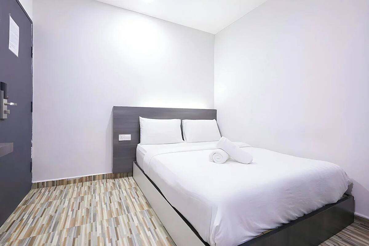 A modern hotel room with a bed, a nightstand, and a door.