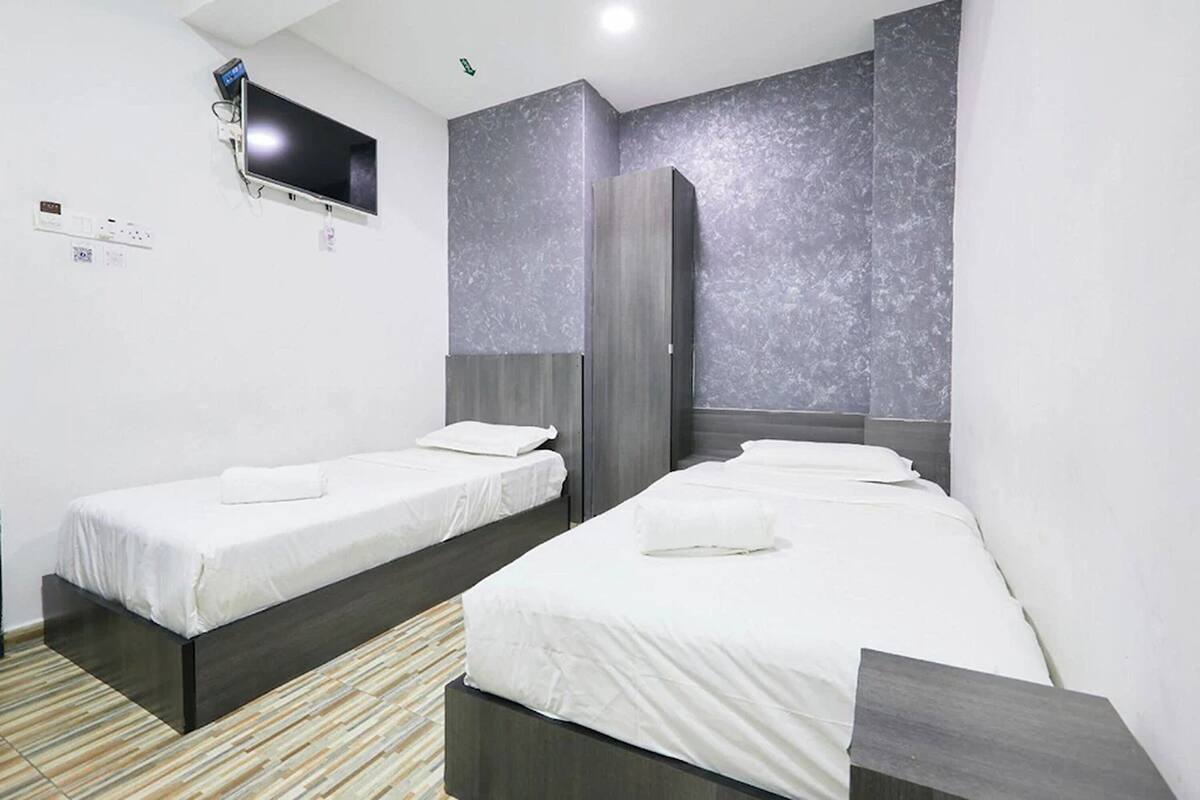 A hotel room with two single beds, a flat-screen TV mounted on the wall, and a wardrobe.