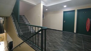 Un escalier avec une rampe verte, un sol carrelé et deux portes vertes portant des numéros.