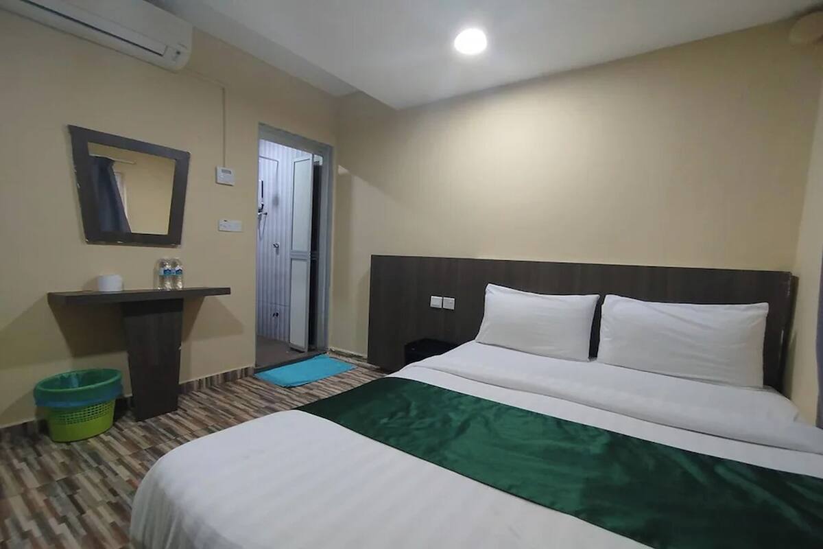 A hotel room with a bed, a bedside table, a mirror, a trash bin, and a door.