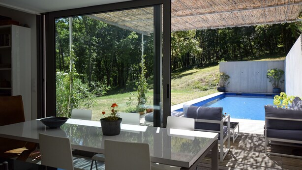 A modern dining area with a glass table, white chairs, and a view of a swimming pool and garden. - Holiday Home in Boissières with Private Pool (Boissieres)