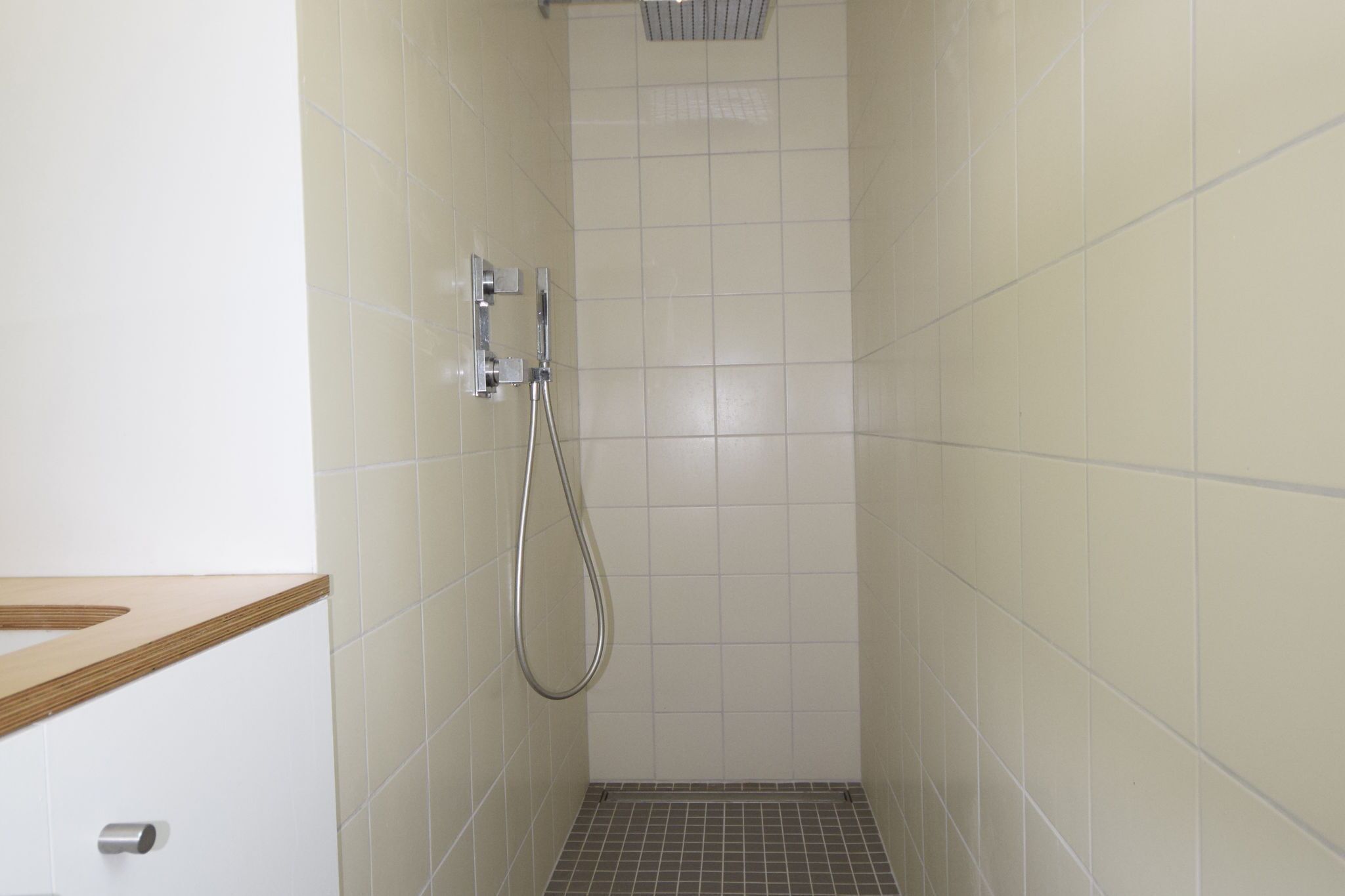 A small, tiled shower area with a showerhead and control panel.