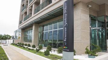 A modern building with a glass facade, a sign indicating 'Narrow Galaxy Place', and a landscaped area with small trees and shrubs.