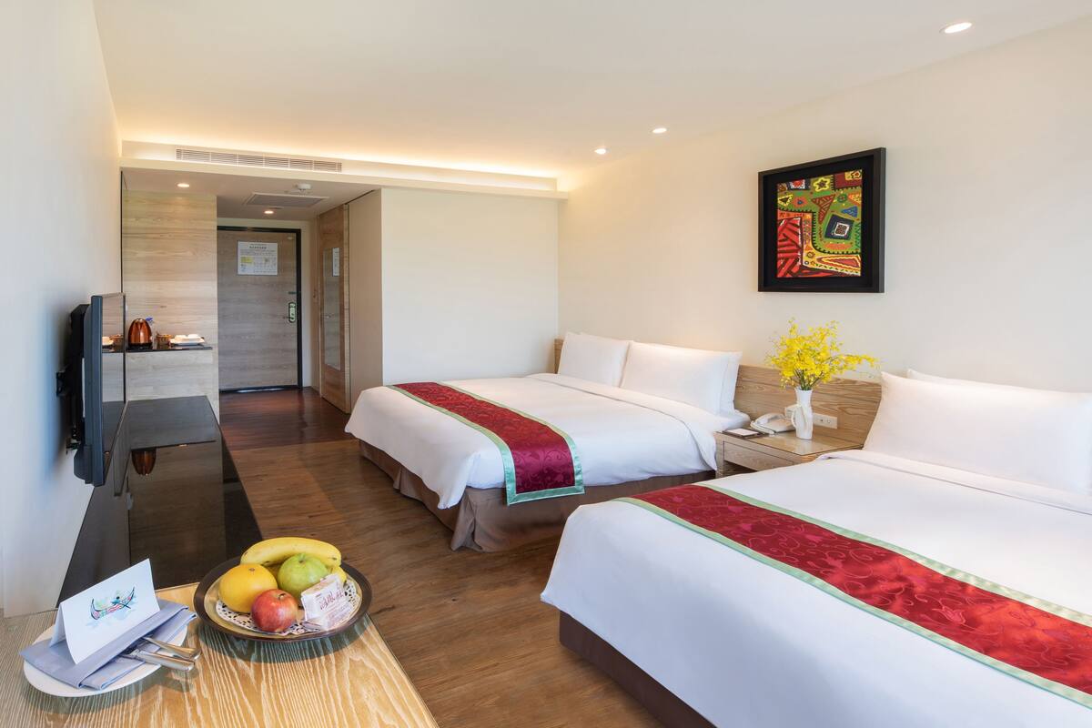 Habitación de hotel con dos camas, televisión, escritorio con computadora y frutero.