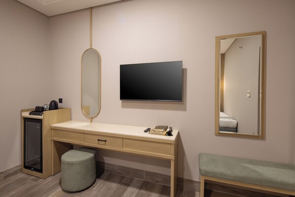 Habitación de hotel con escritorio de madera, televisor de pantalla plana, espejo, banca y minibar.