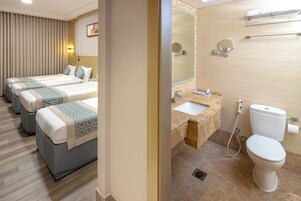 A hotel room with three beds, a bathroom with a sink, toilet, and a mirror.