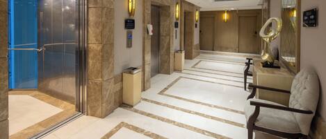 A hotel lobby with a marble floor, elevators, and a seating area with a chair.