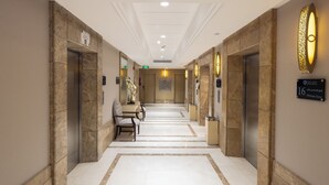 A hotel corridor with marble flooring, wall-mounted light fixtures, and a bench. - Afraa Hotel (Makkah)