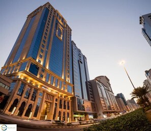 A modern hotel with a prominent glass facade, a classic entrance with arched windows, and a well-lit street scene.