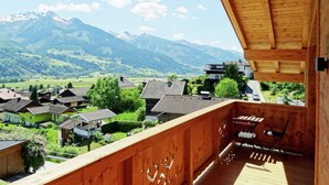 A wooden balcony with a view of a mountain range and a village below.