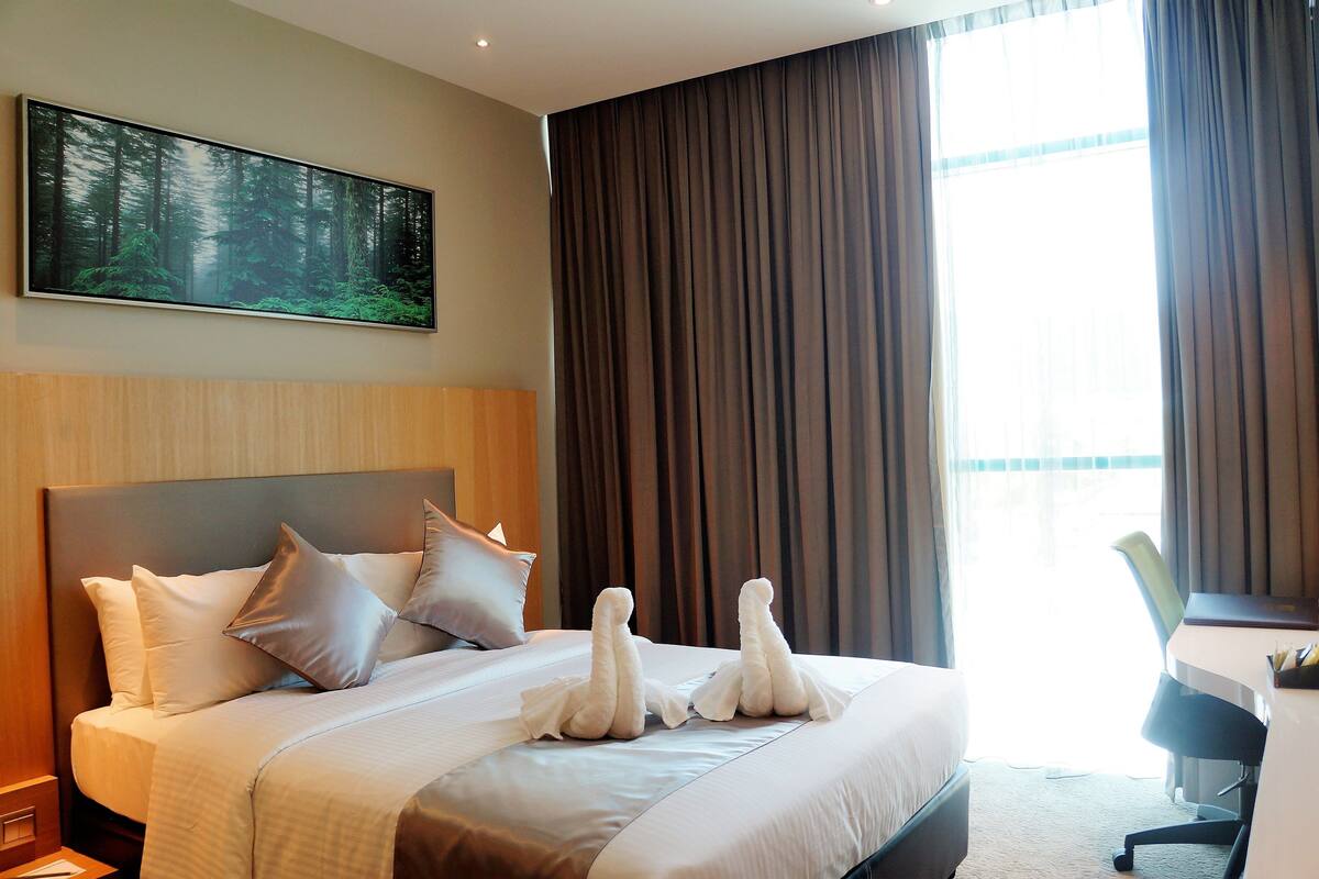 A hotel room with a large bed, a desk, and a painting of a forest on the wall.