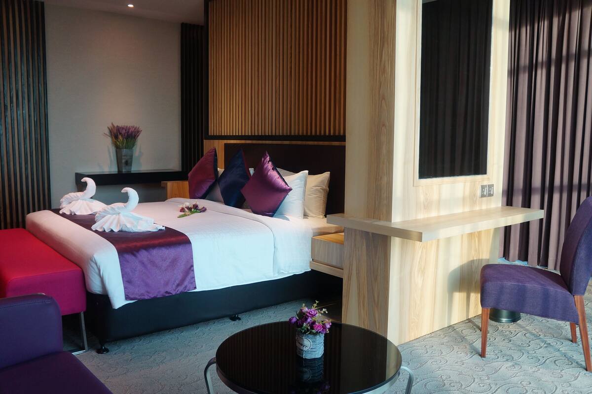 A modern hotel room with a neatly made bed, a small table with a vase of flowers, a desk, and a chair.