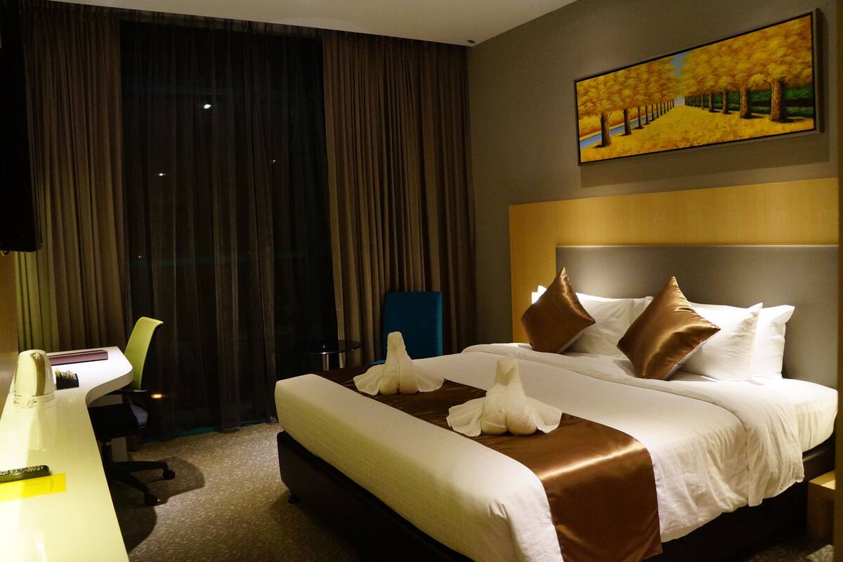 A hotel room with a large bed, a desk, and a chair.